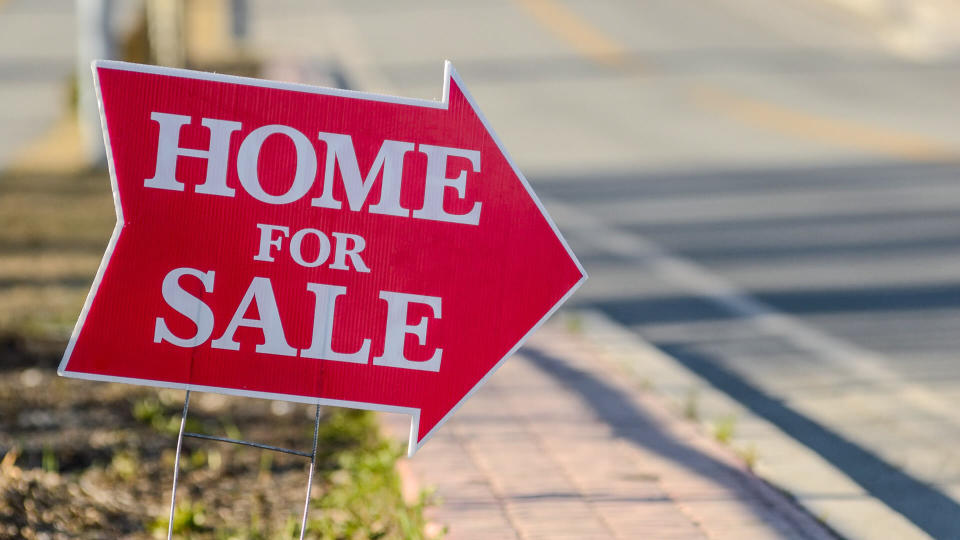 A home for sale sign pointing directing people to a house for sale.