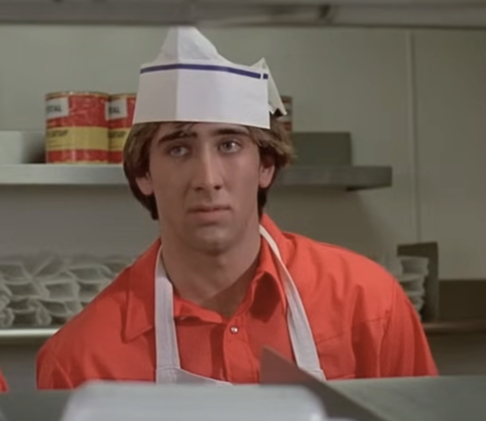 in a scene, Nic in a chef's hat and apron appears concerned in a kitchen setting