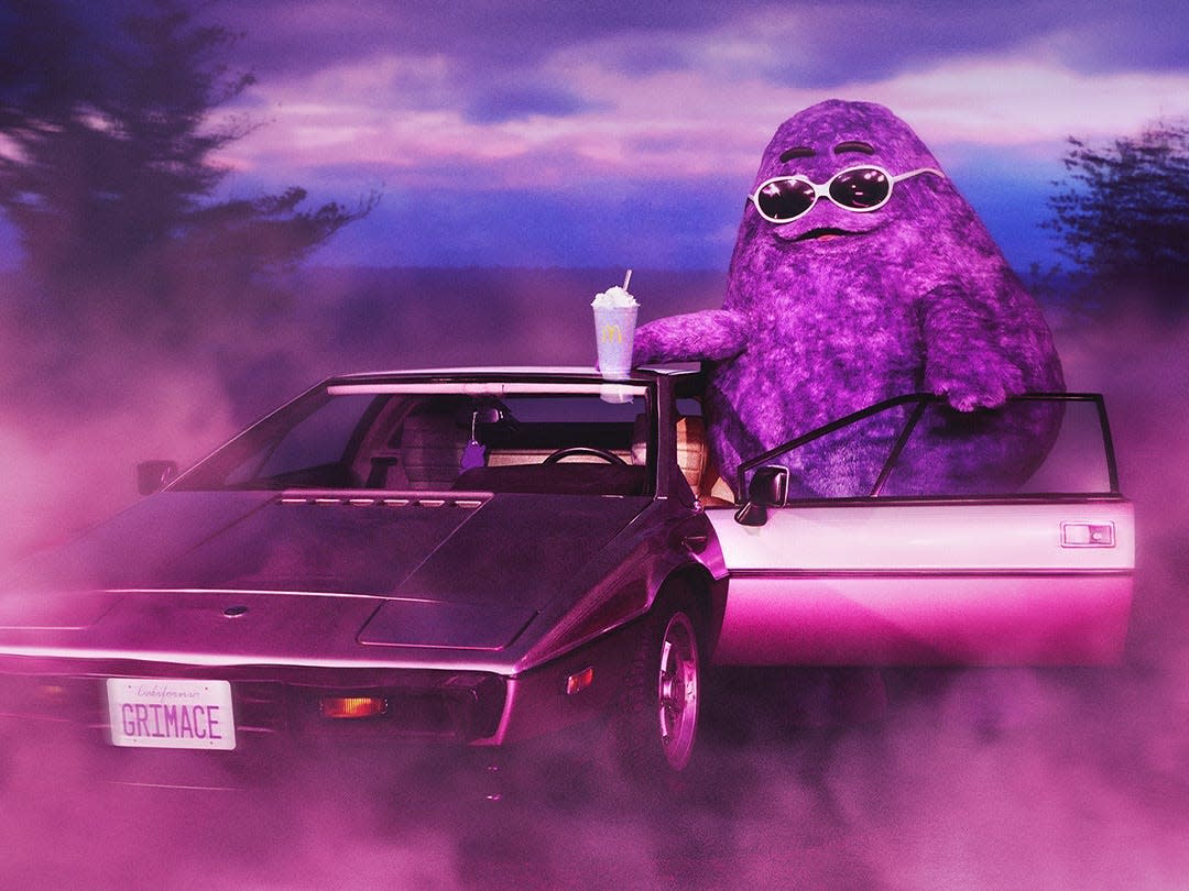 A picture of Grimace wearing sunglasses and holding one of his purple shakes while getting into a car on the way to his birthday party.