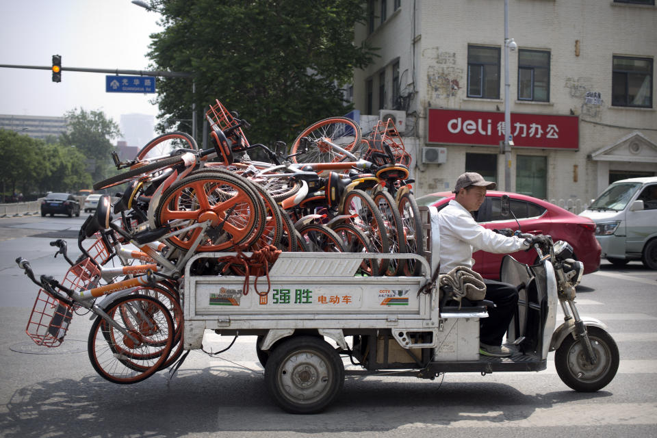 In this Thursday, May 16, 2019, file photo, a worker uses an electric cart to haul a load of ride-sharing bicycles along a street in Beijing. Figures released on Wednesday showed China's factory output and consumer spending weakened in April as a tariff war with Washington intensified, adding to pressure on Beijing to shore up shaky economic growth. (AP Photo/Mark Schiefelbein, File)