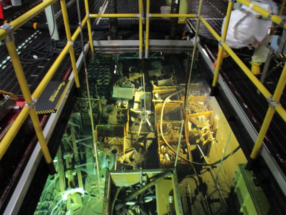 A worker standing on grating above the water in the K Basin Reactor basin sorts debris, a step toward draining contaminated water from the basin.