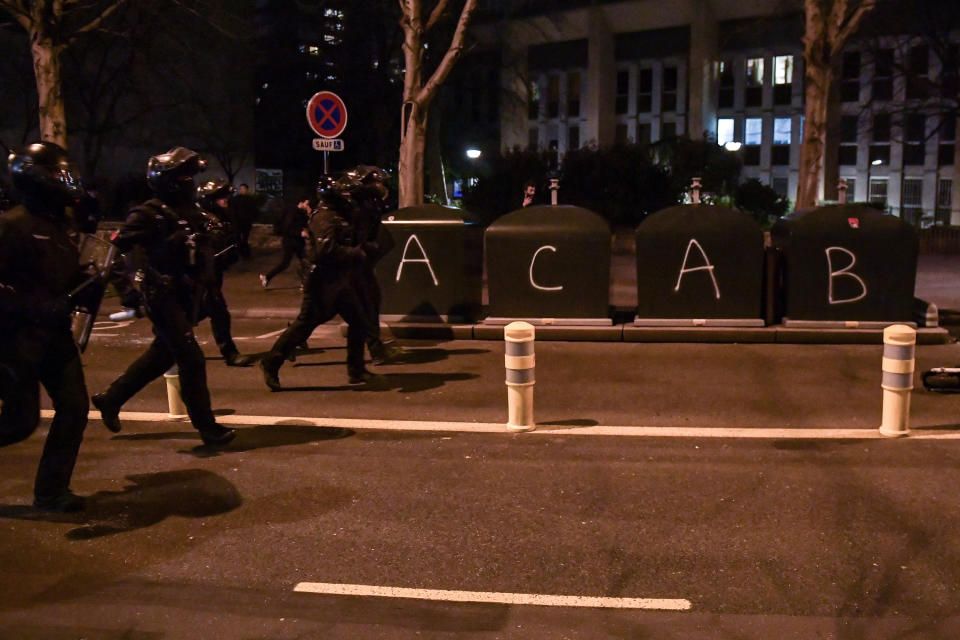 Riot police run down the street that has been vandalized with the tag "ACAB"