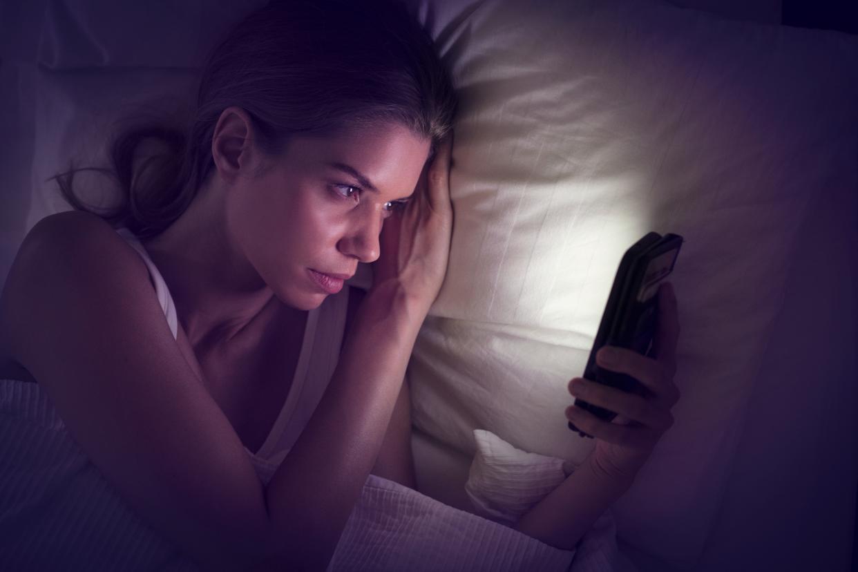 Young woman looking at smartphone in bed.