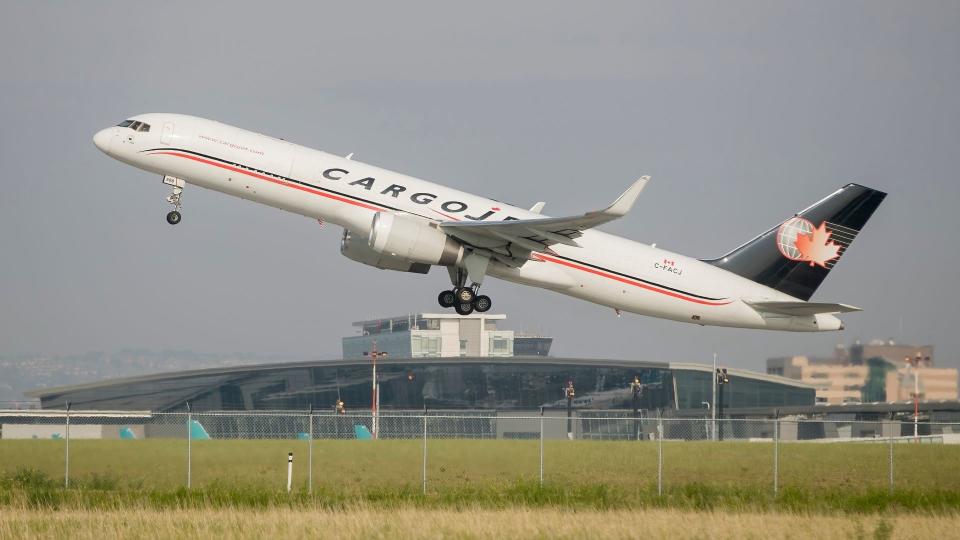 A blue-tailed Cargojet aircraft lifts off the runway, with airport terminal in the background.