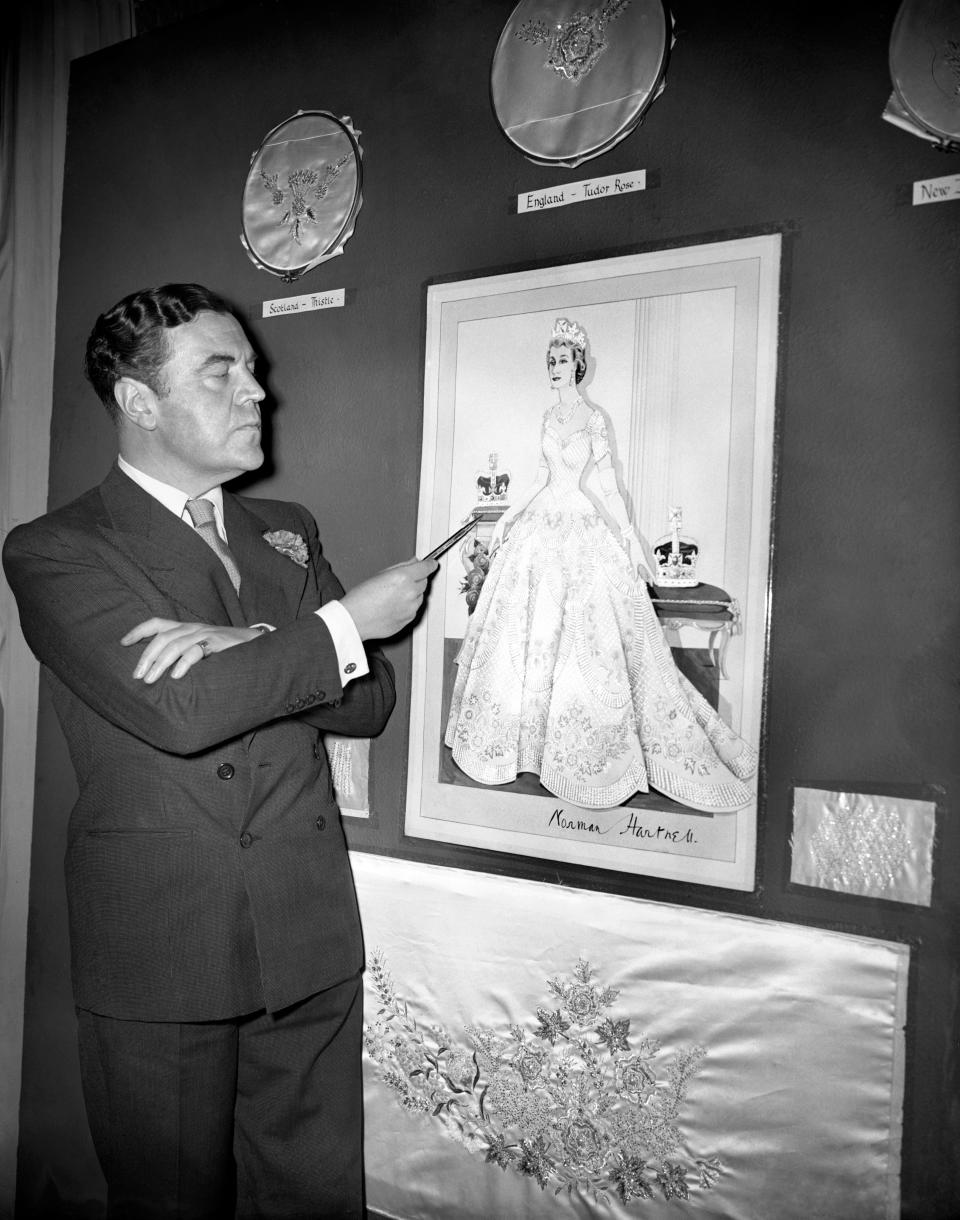 Norman Hartnell, the Royal fashion designer, pointing out the finer points of the Coronation dress he has designed for Queen Elizabeth the Second.   (Photo by PA Images via Getty Images)