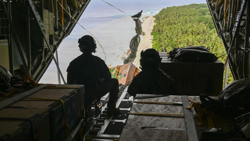 U.S. Air Force Staff Sgt. Matthew Muravez and Senior Airman Megan Irvin, loadmasters with the 36th Airlift Squadron, Yokota Air Base, Japan, push packages over the island of Nama, Dec. 4, as part of Operation Christmas Drop 2023. (Senior Airman Allison Martin/Air Force)