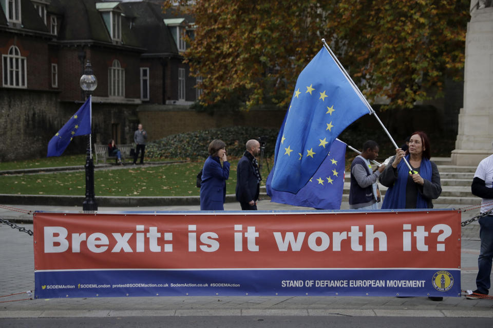 An anti-Brexit supporter holds a European flag by a banner across the street from the Houses of Parliament in London, Thursday Nov. 15, 2018. Leading Brexiteer Jacob Rees-Mogg has submitted a letter of no confidence in Theresa May, as the Prime Minister reels from the loss of four ministers - including two from her Cabinet - in protest at her Brexit plans. (AP Photo/Matt Dunham)