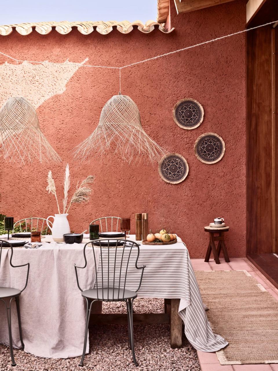 an outdoor table with a white tablecloth and chairs in front of a terracotta painted wall with basket art