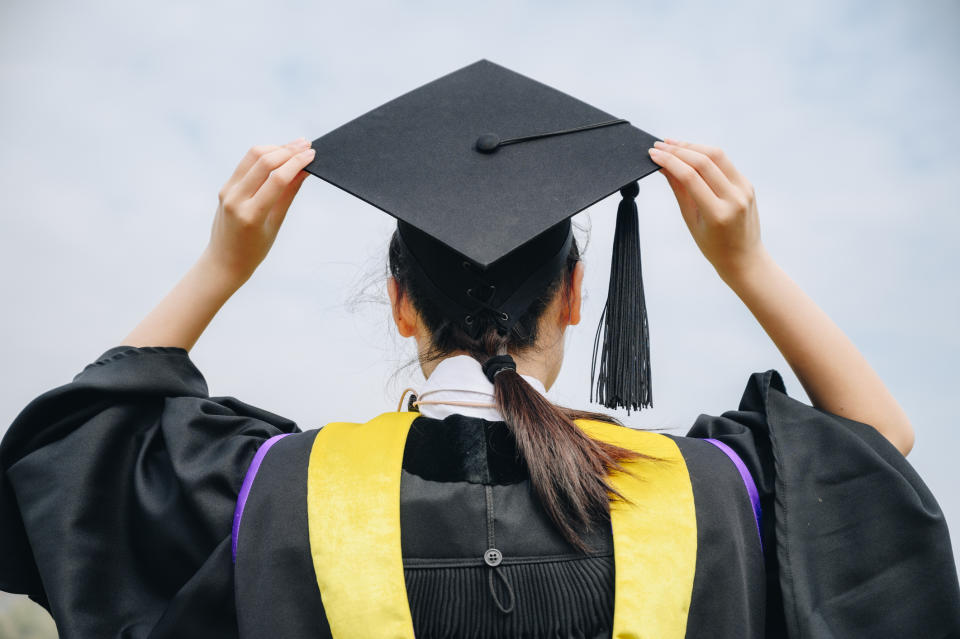 Graduate in cap and gown holding up mortarboard from behind, symbolizing academic achievement and future career potential