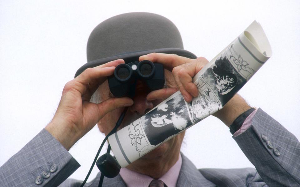 A man in a bowler hat uses binoculars to watch the 1988 Prix de Diane Hermes horse show