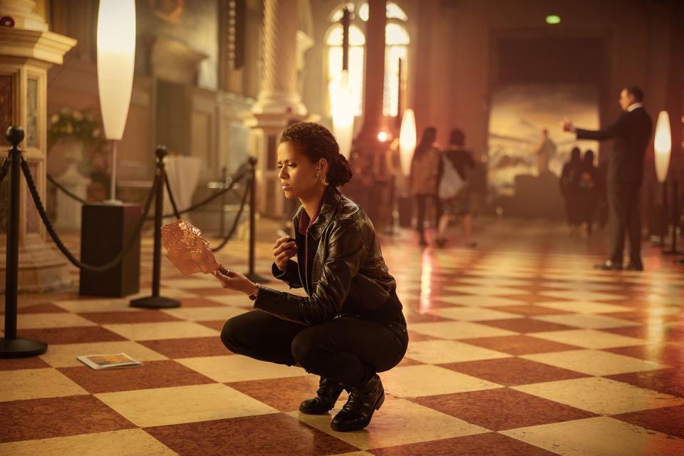 gugu mbatharaw as abby kneeling down holding a gold mask, lift