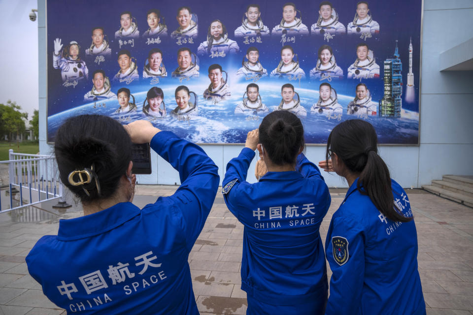 Staff members take photos of a billboard depicting Chinese astronauts at the Jiuquan Satellite Launch Center in northwest China on Monday, May 29, 2023. China's space program plans to land astronauts on the moon before 2030, a top official with the country's space program said Monday. (AP Photo/Mark Schiefelbein)