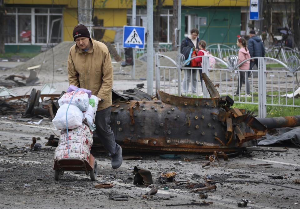 Resident walk past damaged military vehicle in Mariupol