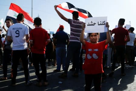 A girl holds a banner that reads "we are all PMF" during a protest against an order for the Popular Mobilization Forces to leave checkpoints in Mosul