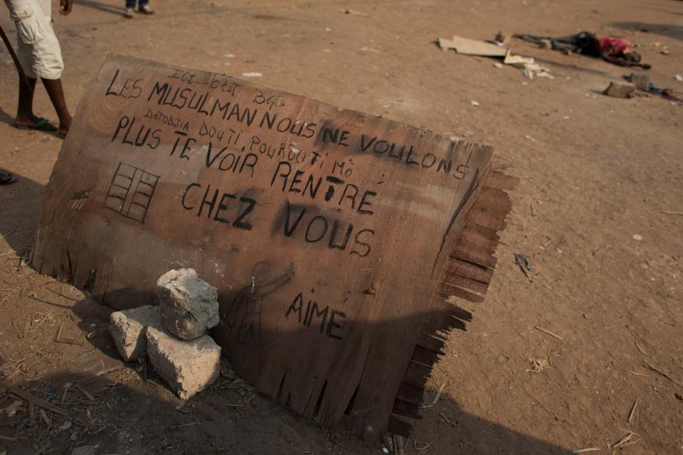 FILE - In this Tuesday, Dec. 31, 2013 file photo, the lifeless body of a man said to be Muslim lies near a sign reading 'We don't want to see any more Muslims here. Go home' in a neighborhood controlled by a squad of local residents, who say they are not anti-balaka but a neighborhood defense squad, armed with machetes, knives, and grenades in Bangui, Central African Republic. Central African Republic has long teetered on the brink of anarchy, but the new unrest unleashed by a March 2013 coup has ignited previously unseen sectarian hatred between Christians and Muslims. The crisis has forced some to flee across borders to desperately poor and unstable countries like Chad and Congo. (AP Photo/Rebecca Blackwell, File)