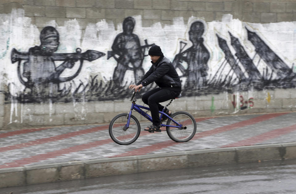 A Palestinian rides his bicycle near graffiti of rockets and militants in Gaza City, in the northern Gaza Strip, Thursday, March 13, 2014. Gaza militants resumed their rocket fire toward Israel on Thursday, striking the outskirts of two major cities a day after launching the largest barrage since an eight-day Israeli offensive in late 2012. Gaza militant groups said they resumed their rocket fire in response to what they say are Israeli "provocations" and violations of a cease-fire, including an airstrike that killed three Islamic Jihad militants earlier this week. (AP Photo/Adel Hana)