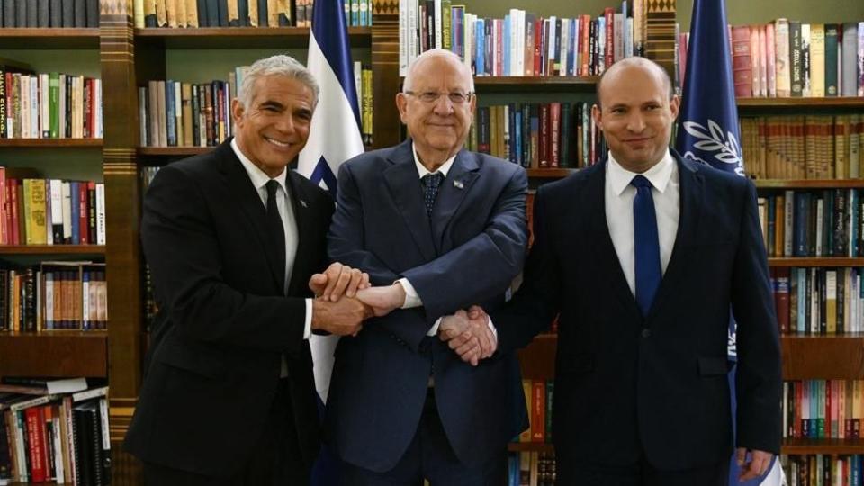 El presidente israelí Reuven Rivlin sosteniendo la mano del nuevo primer ministro Naftali Bennett (derecha) y del Ministro de Relaciones Exteriores Yair Lapid.