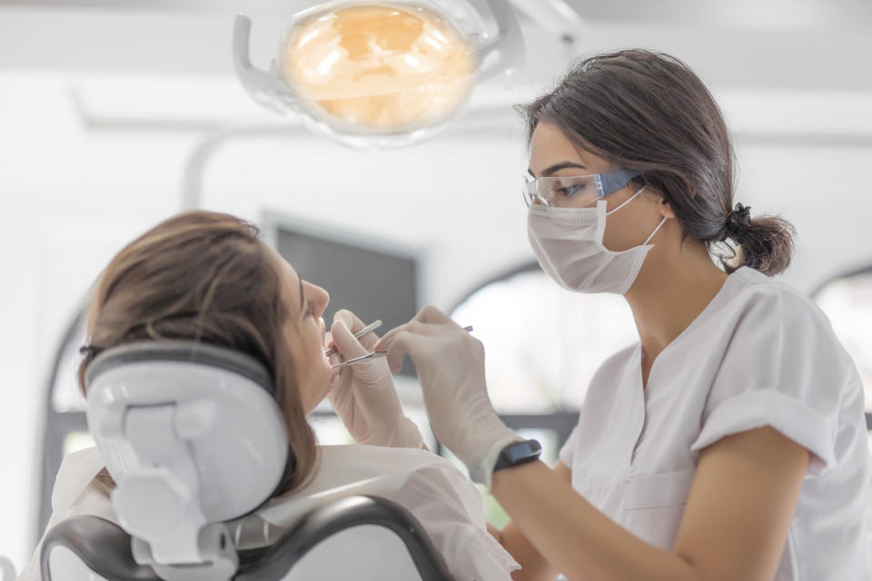 A dental hygienist is cleaning a patient's teeth in a modern dental office. Both are wearing protective masks