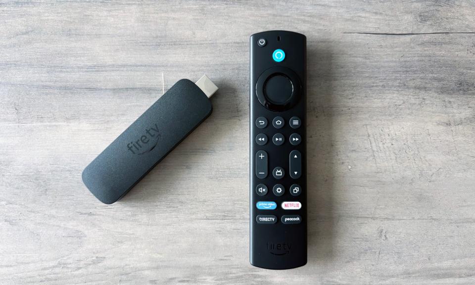 El Amazon Fire TV Stick 4K Max descansa sobre una superficie de madera marrón junto al control remoto incluido.