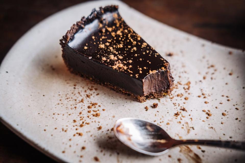 slice of flourless chocolate cake with cocoa powder on top next to a spoon with one bite taken out of it