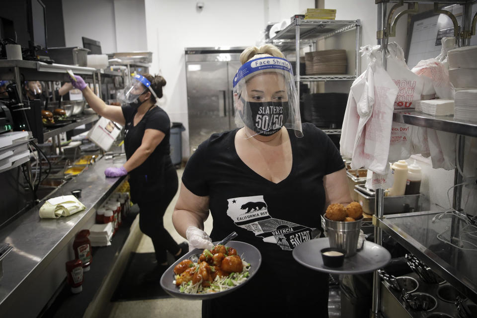 A waitress takes a food order from the kitchen at Slater's 50/50 Wednesday, July 1, 2020, in Santa Clarita, Calif. California Gov. Gavin Newsom has ordered a three-week closure of bars, indoor dining and indoor operations of several other types of businesses in various counties, including Los Angeles, as the state deals with increasing coronavirus cases and hospitalizations. (AP Photo/Marcio Jose Sanchez)