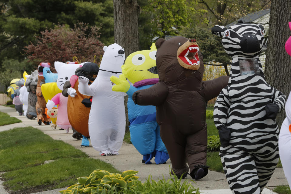 In this Monday, May 11, 2020 photo, members of the T-Rex Walking Club walk through a neighborhood in Ferndale, Mich. While the club members get a kick out of their strolls through town, the idea is to bring a little bit of cheer to their fellow residents who remain under quarantine as part of Gov. Gretchen Whitmer’s stay-at-home order due to the COVID-19 pandemic. (AP Photo/Carlos Osorio)