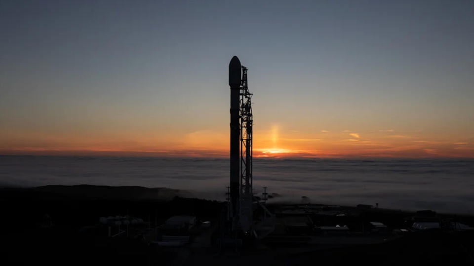 a rocket stands on the pad with the ocean and a sunset sky in the background