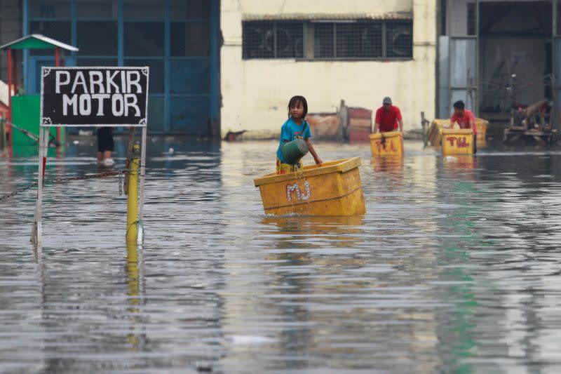 A child stands in a fish storage box at a flooded area affected by land subsidence and rising sea level in North Jakarta