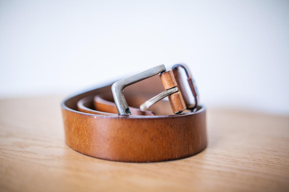 A coiled leather belt with a metal buckle is lying on a wooden surface. No text or people in the image