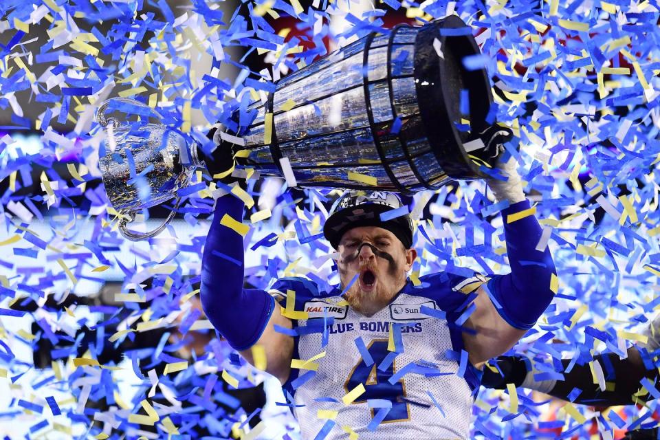 Winnipeg Blue Bombers football player holds up grey cup as confetti rains down