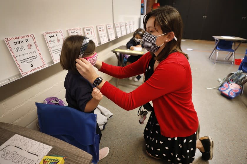 LONG BEACH, CA - OCTOBER 26: Transitional kindergarten and kindergarten teacher Heather Hernandez helps Amelia Dunn with her mask in the classroom as roughly 40 students returned to St. Maria Goretti Catholic School in Long Beach for in-person instruction Monday with transitional kindergarten and kindergarten returning for full-time in-person instruction and 1st and 2nd grade students adopting a hybrid schedule. St. Maria Goretti is the first Catholic School in Los Angeles County to receive waiver approval to reopen since schools moved to remote learning in March due to the COVID-19 pandemic. St. Maria Goretti Catholic School on Monday, Oct. 26, 2020 in Long Beach, CA. (Al Seib / Los Angeles Times