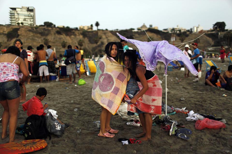 In this Jan. 13, 2013 photo, girls dress under a damaged umbrella on Agua Dulce beach in Lima, Peru. While Lima's elite spends its summer weekends in gate beach enclaves south of the Peruvian capital, the working class jams by the thousands on a single municipal beach of grayish-brown sands and gentle waves. The only barrier to entry to Agua Dulce beach is two dollars, the price of bus fare to get there and home. (AP Photo/Rodrigo Abd)