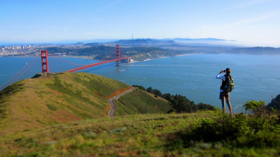 a woman taking a picture of the golden gate bridge, from a hiking viewpoint above san francisco in the marin headlands in california