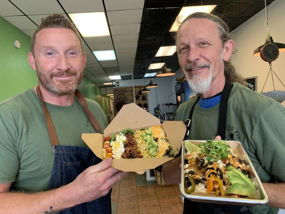 Farm To Fit's co-chefs Kevin Alexander, left, and Brady Privat, hold up a couple freshly prepared meals to go at their new restaurant/meal prep service in downtown Daytona Beach on Thursday, Sept. 16, 2021. Andrea is holding a Farm House Salad. Privat is holding a chicken enchilada bowl.