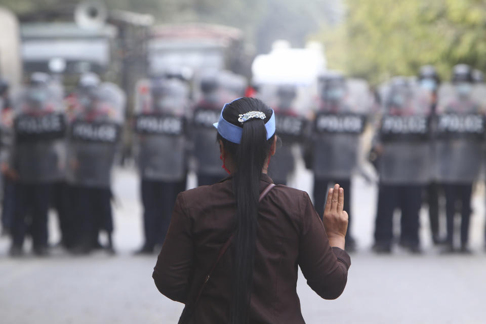 A female protester flashes the three-fingered salute in front of police in Mandalay, Myanmar, Saturday, Feb. 20, 2021. Security forces in Myanmar ratcheted up their pressure against anti-coup protesters Saturday, using water cannons, tear gas, slingshots and rubber bullets against demonstrators and striking dock workers in Mandalay, the nation's second-largest city. (AP Photo)