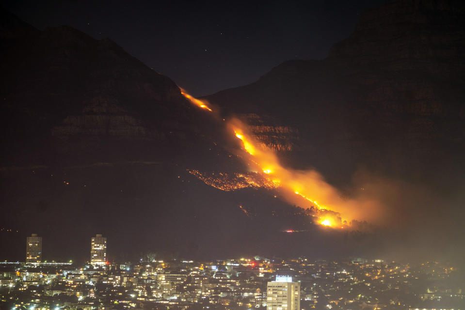 Residential neighborhoods are lit by raging fires in Cape Town, South Africa, Monday, April 19, 2021. Residents are being evacuated from Cape Town neighborhoods after a huge fire spreading on the slopes of the city's famed Table Mountain was fanned by strong winds overnight and threatened houses.(AP Photo/Jerome Delay)