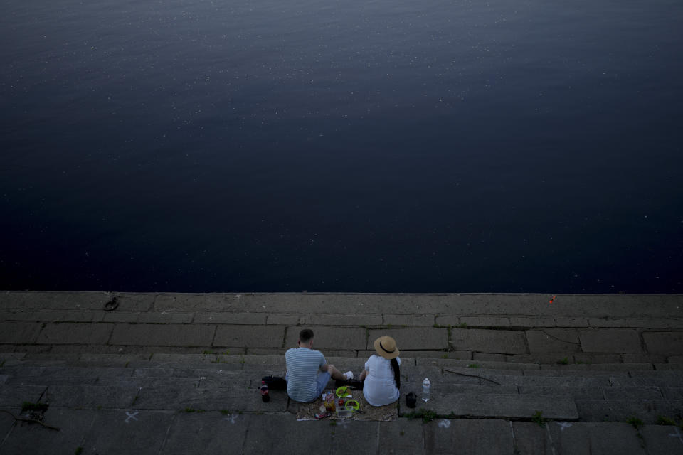 A couple rest in front of the Dnieper River in Kyiv, Ukraine, Friday, June 10, 2022. With war raging on fronts to the east and south, the summer of 2022 is proving bitter for the Ukrainian capital, Kyiv. The sun shines but sadness and grim determination reign. (AP Photo/Natacha Pisarenko)