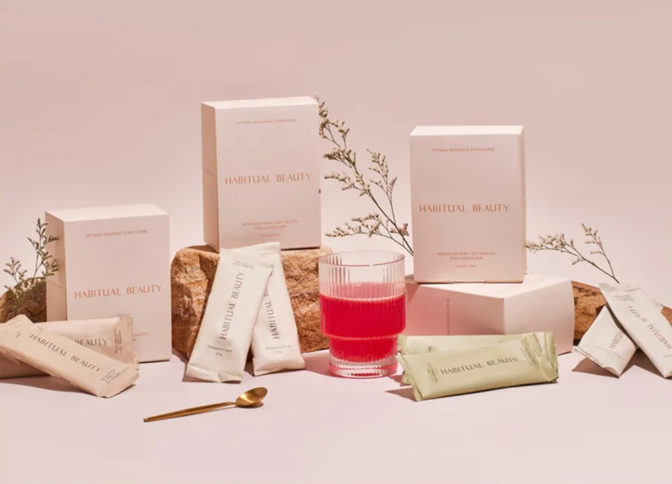 A decorative selection of Habitual Beauty's powdered collagen products arranged on a soft pink background with plant cuttings