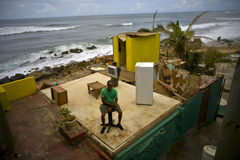 FILE - In this Oct. 5, 2017 file photo, Roberto Figueroa Caballero sits in his home destroyed by Hurricane Maria, two weeks after the storm hit La Perla neighborhood on the coast of San Juan, Puerto Rico. Figueroa, who wanted to stay at home with his dog during the storm, said he was evicted by police and taken to a shelter for the night. When he returned the next day and saw what was left of his home, he decided to put his salvageable items back where they originally were, as if his home still had walls, saying that it frees his mind. (AP Photo/Ramon Espinosa, File)