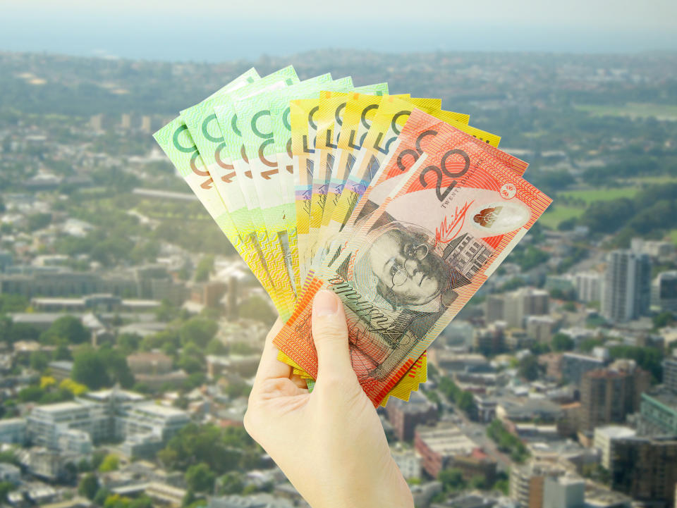 Hand holding Australian cash against Sydney houses backdrop. Image: Getty