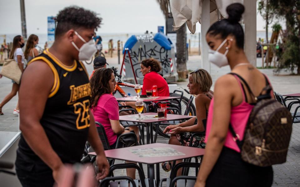 Customers sit at tables outside a bar on the Barceloneta promenade in Barcelona, Spain - Bloomberg