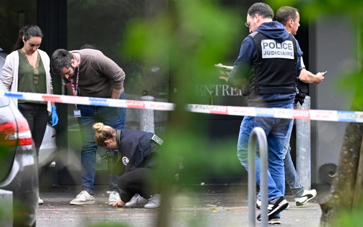 Officers can be seen examining the ground behind police tape