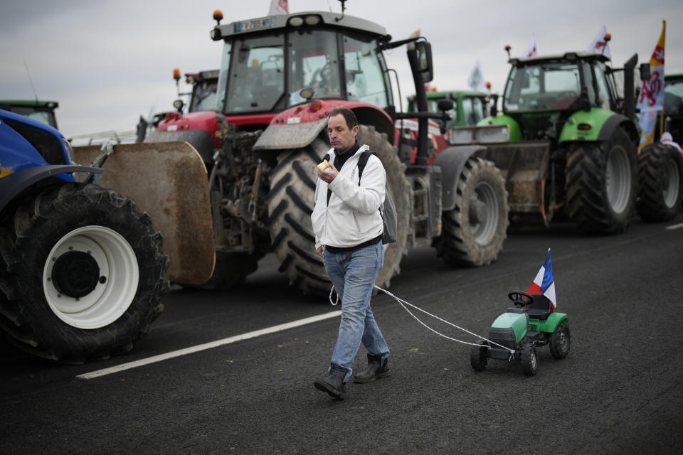 A farmer pulls a toy tractor as farmers block a highway Tuesday, Jan. 30, 2024 in Jossigny, east of Paris. With protesting farmers camped out at barricades around Paris, France's government hoped to calm their anger with more concessions Tuesday to their complaints that growing and rearing food has become too difficult and not sufficiently lucrative. (AP Photo/Christophe Ena)