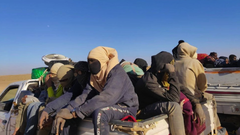 Personas sentadas en la parte trasera de camiones en el desierto sudanés