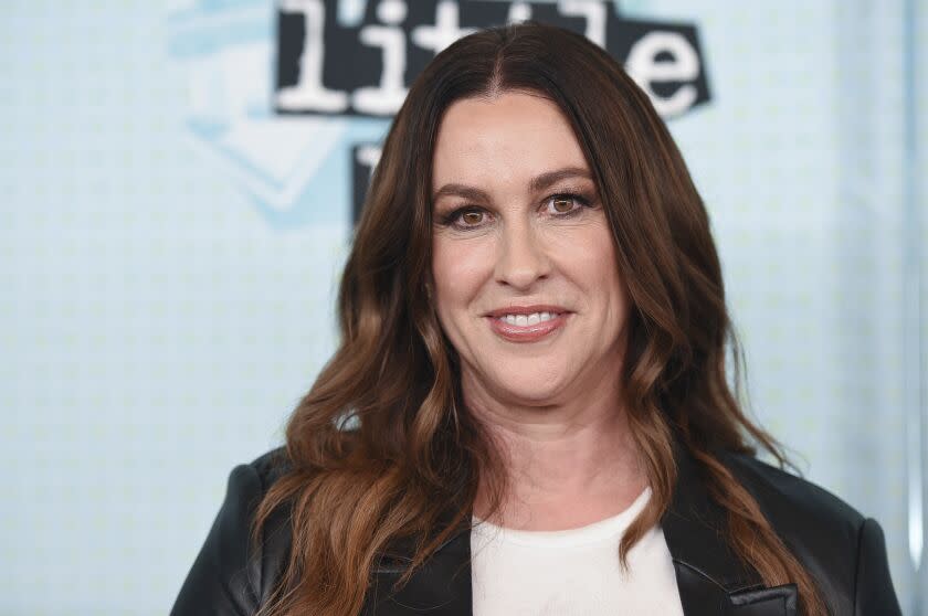 A woman with long brown hair smiling and wearing a black leather jacket