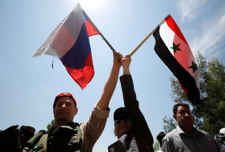 A Russian soldier waves flag with a Syrian woman during the re-opening of the road between Homs and Hama in Rastan, Syria, June 6, 2018. REUTERS/ Omar Sanadiki