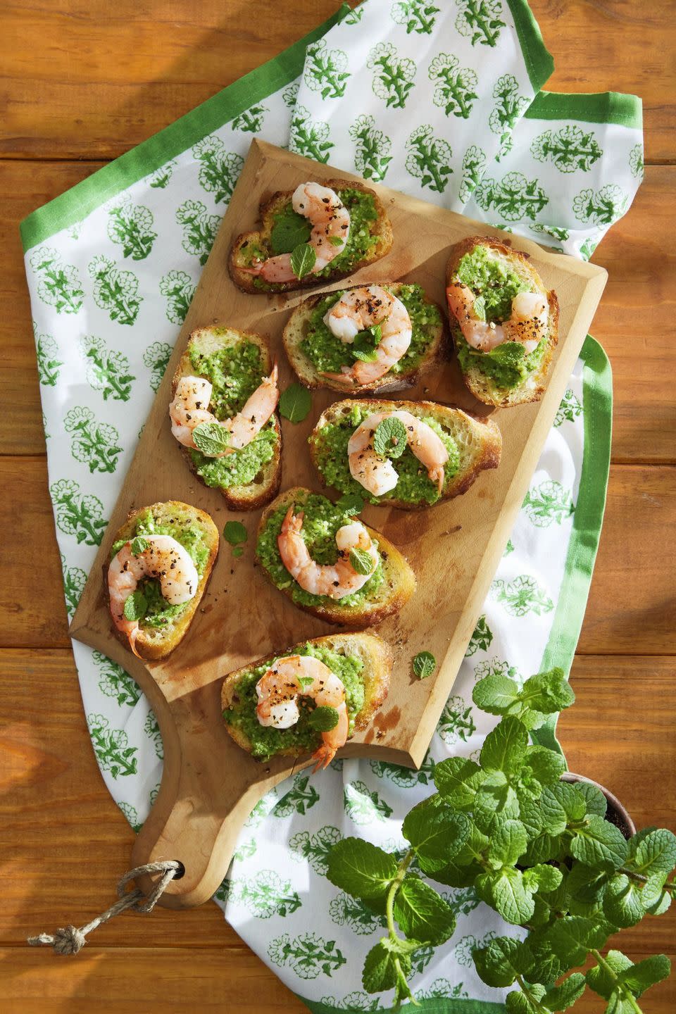 snap pea pesto and shrimp crostini arranged on a wooden serving board