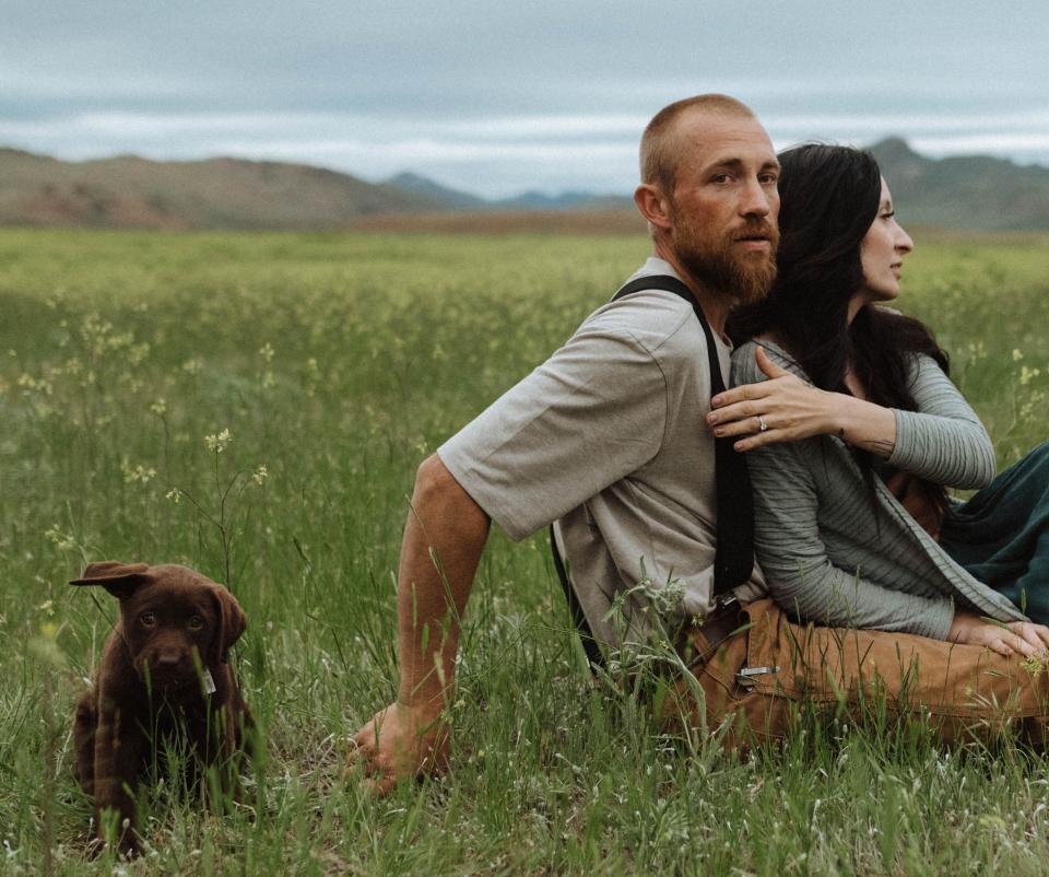 The couple snuggling on the grass with a puppy next to them