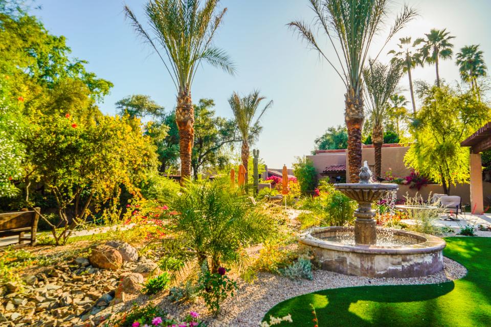 A fountain in front of an adobe building on the left in a garden with succulents, flowers, and palm trees at Hermosa Inn