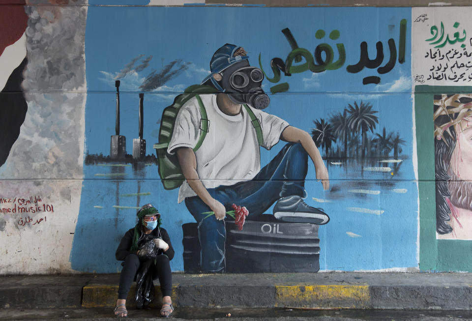 A protester rests by a mural with Arabic that reads "I want my oil," in Baghdad, Iraq, Sunday, Dec. 8, 2019. (AP Photo/Nasser Nasser)